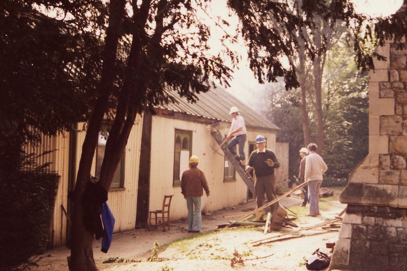 Photo showing the Tin Tab in the first stages of being demolished, with volunteers in hard hats and one on a latter with a pick axe