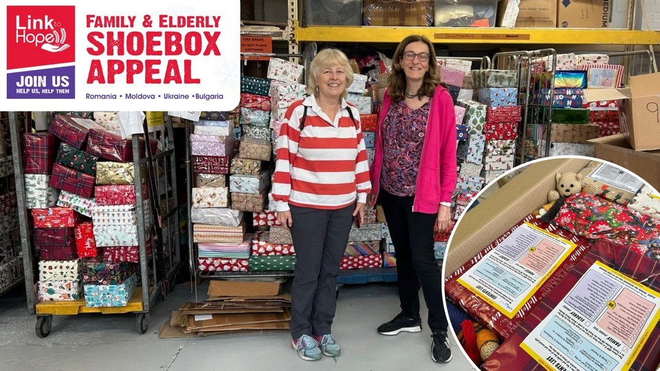 Link to Hope Family and Elderly Shoebox Appeal 2025 - Romania - Moldova - Bulgaria - Ukraine. Helen Cook and Clare Ellensohn are pictured in front of pallets hilding many of the delivered shoeboxes